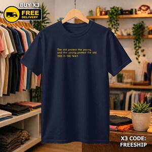 May include: A navy blue t-shirt with yellow text: "The old protect the young, and the young protect the old. THIS IS THE WAY." The shirt is displayed on a wooden hanger. The image also includes a "BUY X3 FREE DELIVERY" graphic.