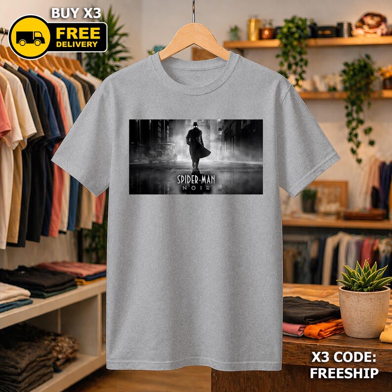 May include: A heather gray short-sleeve t-shirt featuring a rectangular black and white graphic print of a silhouetted figure in a trench coat and fedora walking down a city street with the text Spider-Man Noir printed below the figure.
