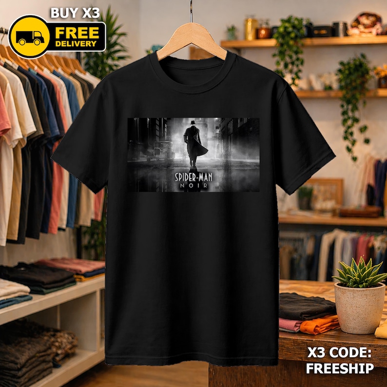 May include: A black short-sleeved t-shirt featuring a rectangular graphic print on the chest. The print displays a black and white scene of a figure in a trench coat and hat standing in a city street, with the text Spider-Man Noir printed below.