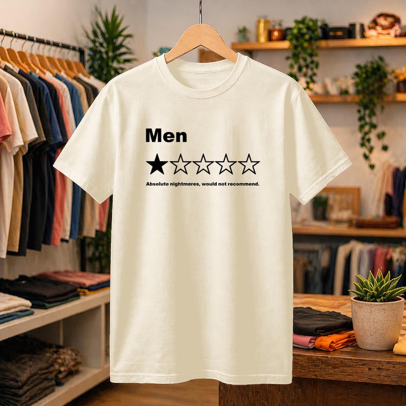 May include: A cream-colored short-sleeve t-shirt featuring the black text 'Men' above a five-star rating graphic with only one star filled in. Below the stars, the black text reads 'Absolute nightmares, would not recommend.'