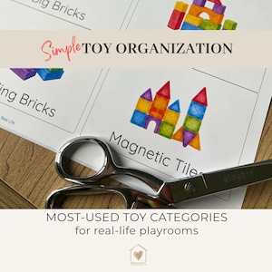 Könnte beinhalten: Ein weißes Blatt Papier mit dem Text Simple TOY ORGANIZATION und MOST-USED TOY CATEGORIES for real-life playrooms, das Abbildungen von bunten Bausteinen und magnetischen Fliesen zeigt und teilweise von einer silbernen Metallschere bedeckt ist.