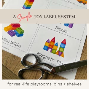 Pode incluir: Uma folha de etiquetas de brinquedos com ilustrações de blocos de construção e azulejos magnéticos. O texto diz "A Simple Toy Label System" e "for real-life playrooms, bins + shelves." Uma tesoura está em primeiro plano.