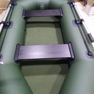 K&ouml;nnte beinhalten: Ein olivgr&uuml;nes Schlauchboot mit zwei schwarzen Sitzb&auml;nken, einem strukturierten olivgr&uuml;nen Boden und zwei silbernen Rudern mit schwarzen Bl&auml;ttern an den Seiten. Eine schwarze Motorhalterung befindet sich am Heck des Bootes.