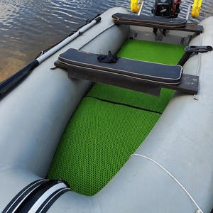 K&ouml;nnte beinhalten: Ein aufblasbares graues Gummiboot mit einer leuchtend gr&uuml;nen Bodenmatte im Wabenmuster, zwei schwarzen Sitzb&auml;nken mit wei&szlig;er Kante und einem kleinen Au&szlig;enbordmotor am Heck, der mit zwei gelben R&auml;dern f&uuml;r den Transport ausgestattet ist.