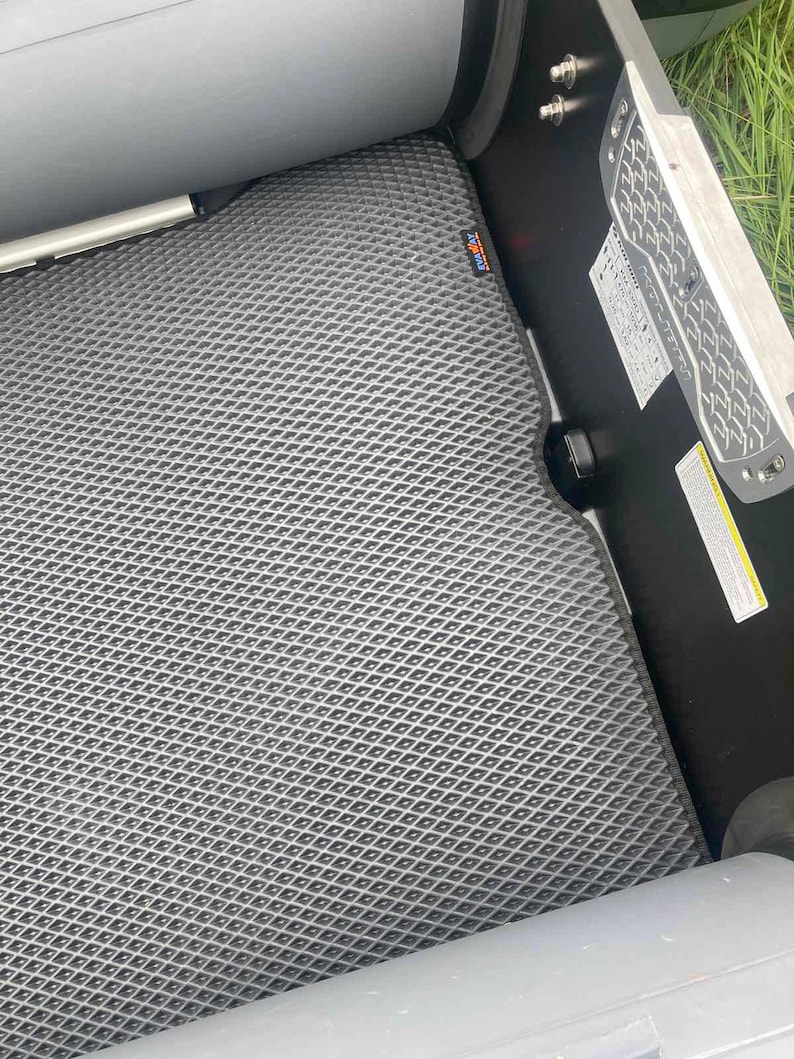 K&ouml;nnte beinhalten: Eine dunkelgraue Bodenmatte mit rautenf&ouml;rmigem Gittermuster, die im Inneren eines Bootes installiert ist. Die Matte verf&uuml;gt &uuml;ber ein kleines rechteckiges Etikett mit dem Text EVAWAY. Eine schwarze Seitenwand mit wei&szlig;em Aufkleber ist sichtbar.