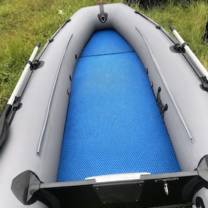 K&ouml;nnte beinhalten: Ein Schlauchboot mit hellgrauen Schl&auml;uchen und einer leuchtend blauen, strukturierten Bodenmatte. Das Boot verf&uuml;gt &uuml;ber schwarze Ruderdollen, seitliche Halteleinen und einen schwarzen Heckspiegel. Der Boden ist mit einer blauen Anti-Rutsch-Matte ausgelegt.