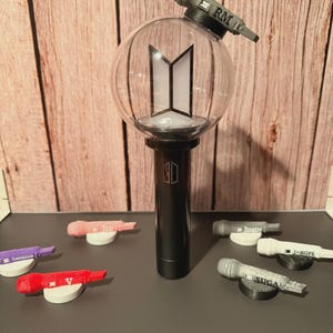 May include: A black and clear light-up sphere with a black base and a miniature microphone on top. The sphere has a white logo inside. Several miniature microphones with different names are on the surface.
