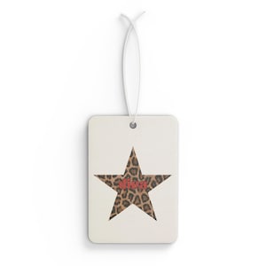 May include: A rectangular air freshener with a white background. A leopard print star is centered on the front, with the word "diva" in red letters. A white string is attached for hanging.