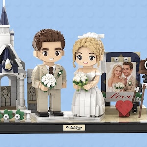 May include: A building block set featuring a bride and groom figurine, a white church structure, a vintage-style camera on a tripod, and a framed photograph of a couple with the word Love printed below. The base has a plaque labeled Wedding.