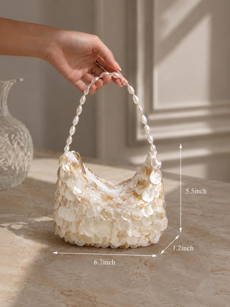 May include: A small handbag covered in iridescent white circular shell-like discs with a handle made of white beads. The bag measures 6.7 inches in width, 5.5 inches in height, and 1.2 inches in depth, featuring a top zipper closure.