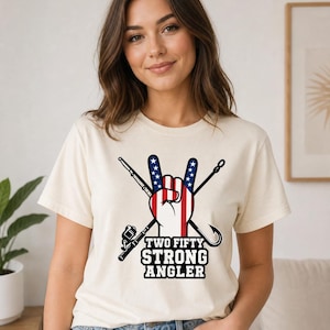 May include: A cream-colored short-sleeve t-shirt featuring a graphic of a hand making a peace sign with an American flag pattern. Behind the hand are crossed fishing rods and hooks. The text "TWO FIFTY STRONG ANGLER" is printed in black below.