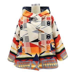 May include: A hooded coat featuring a cream base with a geometric pattern in orange, red, black, and blue. The coat includes long sleeves, two front pockets, and three wooden toggle closures down the front, displayed on a mannequin torso.