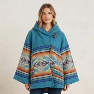 May include: A teal hooded cape featuring a horizontal geometric pattern in shades of orange, blue, and cream. The garment has wide sleeves and is secured at the front with three wooden toggle closures. The fabric displays a soft, textured finish.