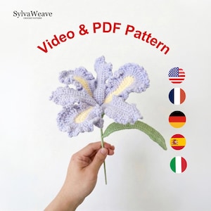 May include: A crocheted iris flower in shades of lavender and yellow, with a green stem and leaf. The image includes the text "Video & PDF Pattern" and the SylvaWeave logo. The flower is held by a person.