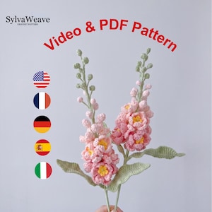 Op de afbeelding: Twee handgemaakte gehaakte bloemen met roze bloemblaadjes en gele centra, groene bladeren en stelen. De tekst "Video & PDF Pattern" is rood. Het SylvaWeave-logo staat linksboven. Vlaggen van de VS, Frankrijk, Duitsland, Spanje en Italië links.