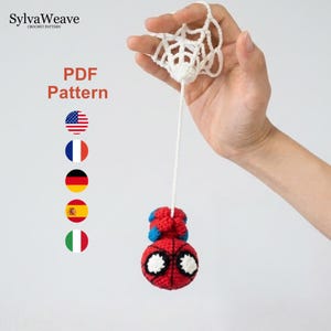 Könnte beinhalten: Eine PDF-Häkelanleitung von SylvaWeave, die eine kleine, runde, rot-blaue Superheldenfigur mit großen weißen Augen zeigt, die an einem weißen gehäkelten Netz hängt. Der Text lautet SylvaWeave Crochet Pattern und PDF Pattern, begleitet von fünf kreisförmigen Nationalflaggen.