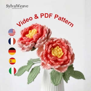 May include: Two handmade crochet flowers in a white vase. The flowers are pink and yellow, with green leaves. The text "Video & PDF Pattern" is in red. The SylvaWeave logo is in the top left corner.