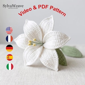 Könnte beinhalten: Eine handgefertigte weiße Häkelblume mit gelben Staubblättern und grünen Blättern. Das Bild enthält den Text "Video & PDF Pattern" und das SylvaWeave Häkelmuster-Logo. Die Blume wird auf einem neutralen Hintergrund dargestellt.