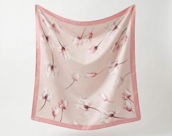 May include: A square, blush-pink scarf with a delicate floral pattern. The scarf features a repeating design of white and pink flowers, framed by a darker pink border. The scarf is made of a silky material.