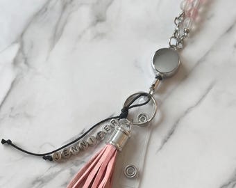 May include: A personalized lanyard with a pink tassel and the name "JENNIFER" spelled out in small letter beads. The lanyard features a retractable reel and a beaded chain with pink and clear beads.