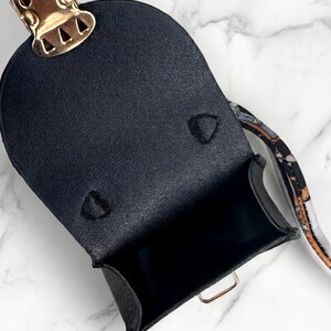 May include: Black leather mini bag with a gold-tone clasp and hardware. The bag has a structured shape and a patterned strap. The interior is black. The bag is open, revealing the inside.