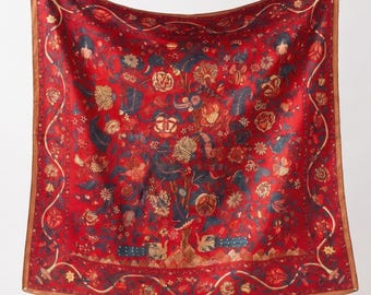May include: A square silk scarf in a vibrant red hue featuring a detailed botanical print with dark blue and gold floral motifs, scrolling vines, and two stylized birds at the base, all framed by a thin brown border along the outer edges.