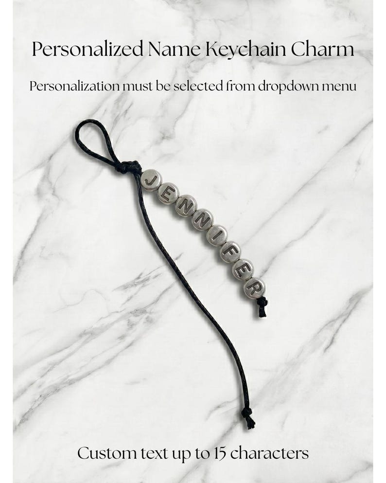 May include: A personalized name keychain charm with the name "JENNIFER" spelled out in silver letter beads. The keychain has a black cord and the text "Custom text up to 15 characters".