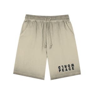 May include: Stone-coloured shorts with a drawstring waist and pockets. The shorts feature the words "PEACE WORLD" printed in black on the lower right leg. The fabric has a faded, vintage appearance.