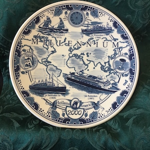 May include: A white ceramic plate with a blue and white design featuring ships, a world map, and the word "MILLENNIUM". The plate includes the text "Holland America 2000" and ship names with dates.