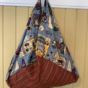 May include: A handmade tote bag with a patchwork design. The upper portion features a light blue fabric with various patterns, while the bottom has a red and brown striped fabric. The bag has a gray handle.