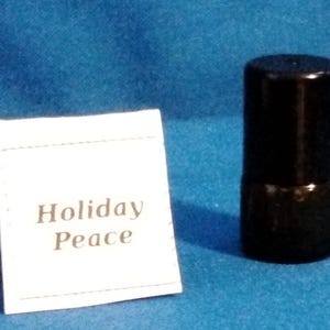May include: A black cylindrical object stands next to a white tag. The tag reads "Holiday Peace" in a serif font. The background is a solid blue color. The cylindrical object appears to be a bottle stopper.