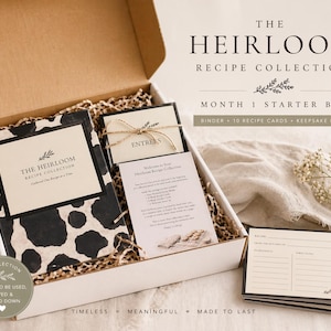 May include: An open box containing a recipe collection starter kit. The kit includes a binder, recipe cards, and keepsake inserts. The binder has a black and white cow print design. The text on the box reads "The Heirloom Recipe Collection".