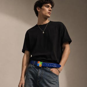 May include: A black t-shirt, blue jeans, and a silver chain necklace. The blue belt features a multi-colored square logo resembling a window pane and digital text displaying 3:30 AM and 10/22/2008 on the strap near the buckle.