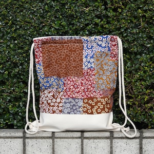 May include: A white drawstring bag with a patchwork design. The patchwork is made of different fabrics with floral patterns in shades of brown, blue, red, and white.