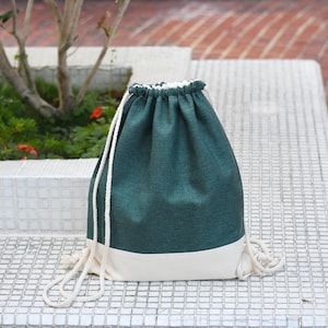 May include: A teal green drawstring bag with a white bottom. The bag is made of a canvas-like material and has white drawstrings.