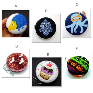 May include: Six different round coin purses with various designs. The purses are made of fabric and have a zipper closure. The designs include a hedgehog, a paisley pattern, an octopus, a crane, a cupcake, and a Halloween theme with pumpkins and spiders.
