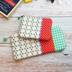 May include: Two fabric zippered pouches with different patterns. The top pouch has a white background with a red floral pattern and a red and white polka dot pattern on the right side. The bottom pouch has a white background with a green and white checkered pattern.