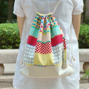 Puede incluir: Una mochila blanca con cordón de ajuste y diseño de patchwork. La tela está hecha de diferentes patrones coloridos, incluyendo rojo, amarillo, verde y azul. La mochila tiene una etiqueta blanca con el texto "silvergreen" en ella.