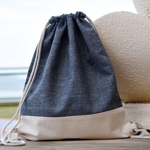 Puede incluir: Una bolsa de cordón azul y blanco hecha de tela texturizada. La bolsa tiene un fondo blanco y una parte superior azul.
