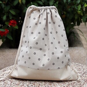 Könnte beinhalten: Eine weiße Kordeltasche mit einem schwarzen Blumenmuster. Die Tasche hat ein weißes Baumwollfutter und eine weiße Kordel.