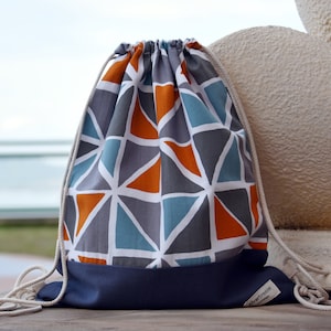 May include: A drawstring bag with a geometric pattern in shades of grey, blue, and orange. The bag has a navy blue bottom and a white drawstring with the text "silverbreeze" printed on a tag.