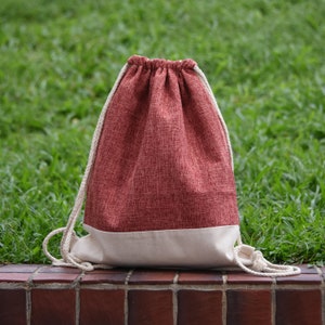Puede incluir: Una bolsa de cordón roja con fondo blanco. La bolsa está hecha de una tela texturizada y tiene un cordón blanco.
