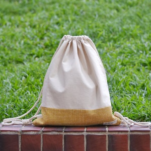 Könnte beinhalten: Eine weiße Kordeltasche mit gelbem Boden. Die Tasche ist aus Naturstoff und hat ein schlichtes Design.