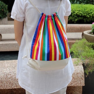 May include: A white drawstring bag with a rainbow striped pattern. The bag is being worn by a person.