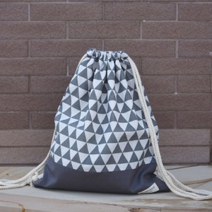 May include: A gray and white drawstring bag with a geometric pattern of triangles. The bag has a gray bottom and white drawstrings.