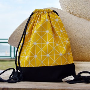 May include: A yellow drawstring bag with a white geometric pattern and a black bottom. The bag has black drawstrings and a black label with the text "silverbreeze" on it.