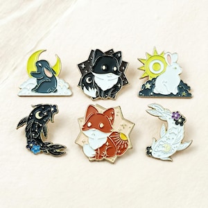 May include: Six enamel pins with celestial and animal designs. The pins feature a black and white cat, a red fox, a black fish, a white rabbit, and a black rabbit. Each pin has a starburst border and is set against a light background.