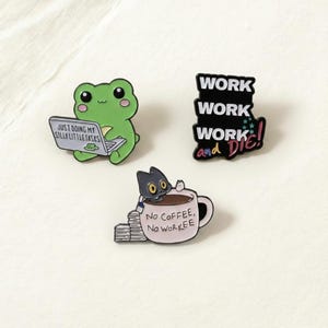 May include: Three enamel pins: a green frog with a laptop, a black pin with the words "WORK WORK WORK and DIE!", and a cat in a coffee cup with the text "No COFFEE, No WORKEE".