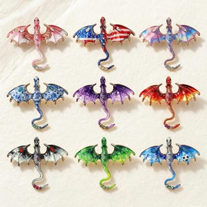 May include: Nine dragon brooches in various colors, including red, blue, purple, and green. Each brooch features detailed wings and a curled tail, with some designs incorporating patterns and gemstones. The brooches are displayed on a light-colored surface.