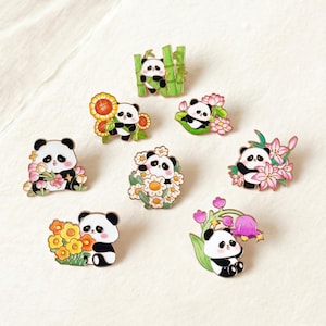 May include: A collection of enamel pins featuring adorable panda bears in various poses. Each pin showcases a panda with different floral or bamboo accents, including sunflowers, lilies, and daisies. The pins have black, white, green, yellow, and pink colors.